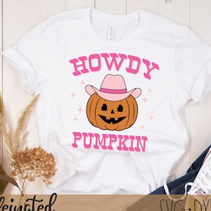 May include: White t-shirt with a pink graphic of a pumpkin wearing a pink cowboy hat. The text "Howdy Pumpkin" is written in pink letters.