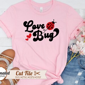 以下が含まれることがあります： レトロなフォントで「Love Bug」というテキストと、黒と赤のテントウムシのグラフィックが描かれたピンクのTシャツです。