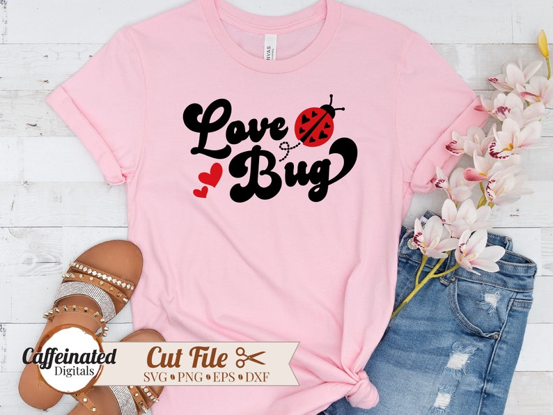 以下が含まれることがあります： レトロなフォントで「Love Bug」というテキストと、黒と赤のテントウムシのグラフィックが描かれたピンクのTシャツです。