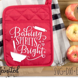 Pu&ograve; includere: Guanto da forno rosso trapuntato con la scritta bianca "Baking Spirits Bright". Il guanto ha una tasca e un anello per appenderlo. Tre mele sono in un vassoio di legno.