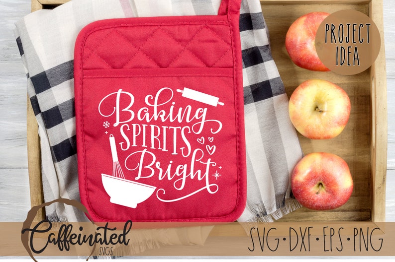 Pu&ograve; includere: Guanto da forno rosso trapuntato con la scritta bianca "Baking Spirits Bright". Il guanto ha una tasca e un anello per appenderlo. Tre mele sono in un vassoio di legno.