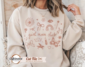 May include: Beige sweatshirt with a collection of whimsical illustrations in a muted rose color. The design includes a flower, bow, rainbow, lipstick, butterfly, and the text "girl mom club". The bottom left corner has the text "Caffeinated Digitals".