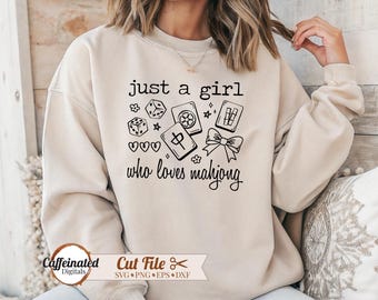 May include: A beige sweatshirt with the text "just a girl who loves mahjong" and graphic illustrations of dice, hearts, and mahjong tiles. The sweatshirt also has a bow graphic and the words "Cut File" with file type icons.