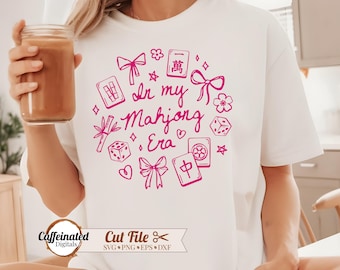 May include: White t-shirt with a pink graphic design featuring the text "In my Mahjong Era" surrounded by Mahjong tiles, dice, and bows. The shirt also has the text "Caffeinated Digitals" and "Cut File" at the bottom.