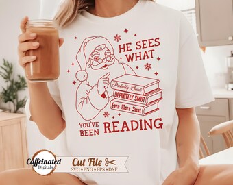 May include: White t-shirt with a red graphic of Santa Claus pointing at a stack of books labeled "Probably Smut," "Definitely Smut," and "Even More Smut." The text "He Sees What You've Been Reading" is also in red.