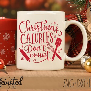 Pu&ograve; includere: Una tazza di ceramica bianca con la scritta "Christmas Calories Don't Count" in rosso. La tazza presenta illustrazioni di un mattarello, una frusta e una spatola. Una scatola regalo rossa e ornamenti sono sullo sfondo.