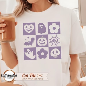 May include: A white t-shirt with a purple design of nine Halloween icons in a grid pattern. The icons include a ghost, a bat, a pumpkin, a spider web, a heart, a flower, and a skull.