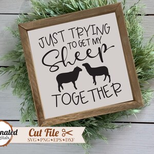 May include: A white wooden sign with the text "JUST TRYING TO GET MY SHEEP TOGETHER" in black lettering. Two black sheep silhouettes are below the text.