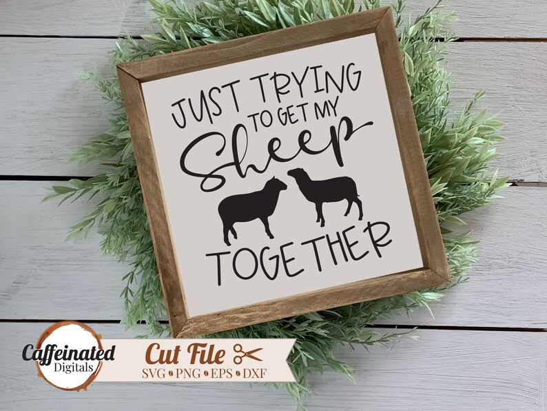 May include: A white wooden sign with the text "JUST TRYING TO GET MY SHEEP TOGETHER" in black lettering. Two black sheep silhouettes are below the text.