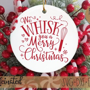 Pu&ograve; includere: Ornamento natalizio in ceramica bianca con testo rosso che recita "We Whisk You a Merry Christmas" e un'illustrazione di una frusta. L'ornamento &egrave; circondato da bacche rosse, verde e bastoncini di zucchero.