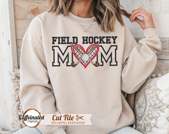 May include: Beige sweatshirt with the text "FIELD HOCKEY MOM" in black block letters. The word "MOM" is in large letters with a red heart in the center, featuring a hockey ball and crossed hockey sticks. The sweatshirt has a crew neck.