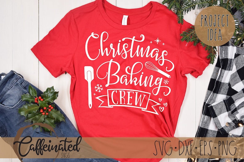 Pu&ograve; includere: Una maglietta rossa con la scritta bianca "Christmas Baking Crew". Il design include una spatola, una frusta, un fiocco di neve e uno striscione. La maglietta &egrave; esposta con jeans, verde e un'etichetta "Project Idea".