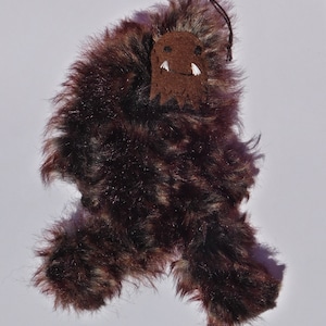 May include: A brown and black furry creature with a brown felt face and white teeth. The creature has a string attached to the top of its head.