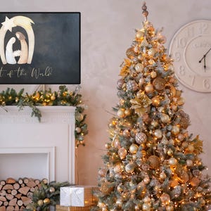 Peut inclure: Un tableau noir avec une illustration aquarelle de la scène de la nativité et le texte "light of the world". Le tableau noir est posé sur une cheminée blanche avec un sapin de Noël décoré de boules dorées et blanches en arrière-plan.