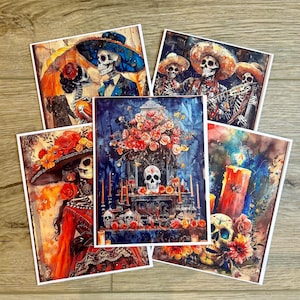 May include: A collection of five square art prints featuring Day of the Dead themes. The illustrations depict skeletons in colorful attire, floral arrangements, and candles in vibrant shades of orange, red, blue, and yellow on a dark background.