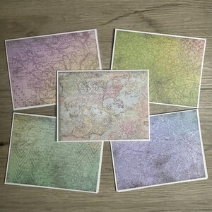 May include: Five rectangular cards featuring vintage-style world map prints in various pastel colors including purple, green, and blue. Each card displays intricate cartographic details, including landmasses, oceans, and grid lines with a weathered texture.