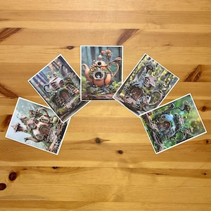 Peut inclure: Cinq impressions d'art représentant des maisons en forme de théières fantaisistes dans des environnements naturels. Les théières sont ornées de détails complexes, comme des portes, des fenêtres et de la verdure miniatures. Les impressions sont disposées sur une surface en bois.