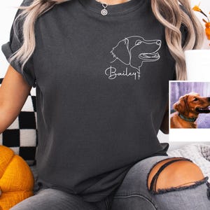 以下が含まれることがあります： 犬の頭の線画と筆記体で「Bailey」という名前が描かれた濃い灰色のTシャツ。ゴールデンレトリバーの小さな写真が背景にあります。このTシャツはカジュアルなスタイルで、普段使いに適しています。