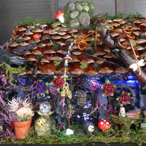 May include: A miniature fairy house made of pine cones, moss, and other natural materials. The house has a blue glass window, a black bird perched on the roof, and a variety of other whimsical details.