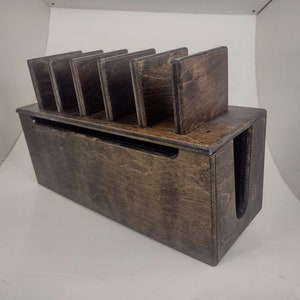 May include: A dark brown wooden organizer with six slots for storing items like coasters or cards. The organizer has a built-in slot for cords or cables.