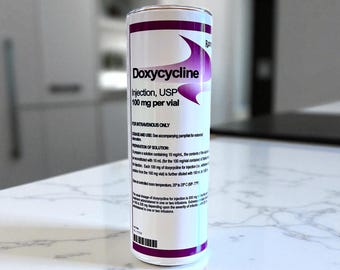 May include: A cylindrical container with the text "Doxycycline Injection, USP 100 mg per vial" in white and purple. The container is for intravenous use only. The background is a blurred kitchen setting.