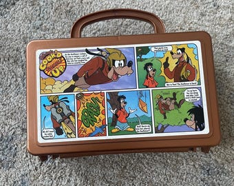 May include: A brown plastic lunchbox with a handle. The lunchbox features a comic strip of Goofy in a pilot's outfit. The comic strip text reads "Goofy's Comic Up".