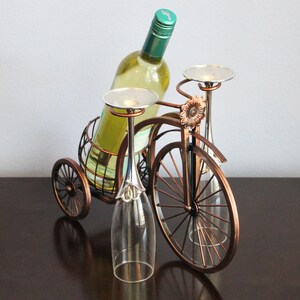 Bronze metal wine bottle and glass holder designed in the shape of a bicycle, holding one wine bottle and two glasses for shared moments, perfect for kitchen displays, dining areas, wine stations, or outdoor picnics, crafted from durable metal with a warm finish, making it a unique wine decor piece and a meaningful gift for weddings, anniversaries, holidays, Valentine’s Day, or housewarming gifts for wine lovers and couples who enjoy thoughtful design