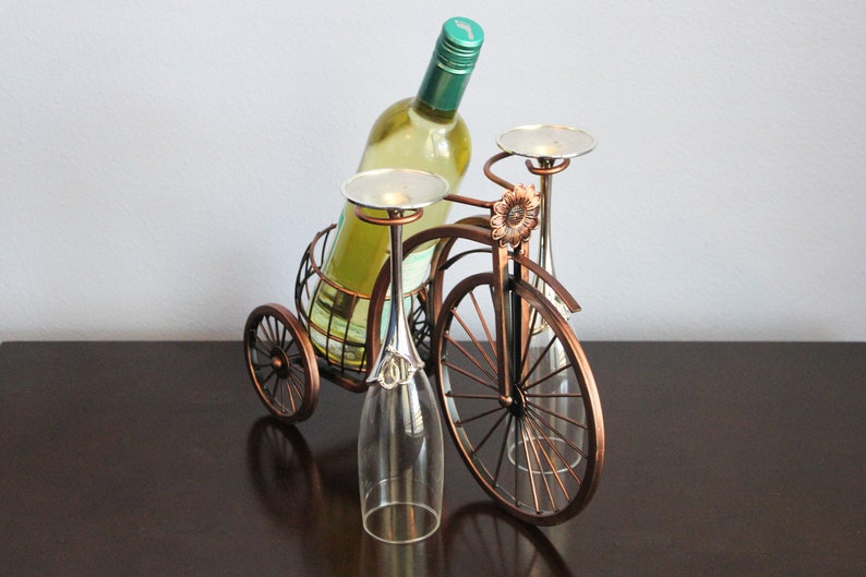Bronze metal wine bottle and glass holder designed in the shape of a bicycle, holding one wine bottle and two glasses for shared moments, perfect for kitchen displays, dining areas, wine stations, or outdoor picnics, crafted from durable metal with a warm finish, making it a unique wine decor piece and a meaningful gift for weddings, anniversaries, holidays, Valentine’s Day, or housewarming gifts for wine lovers and couples who enjoy thoughtful design