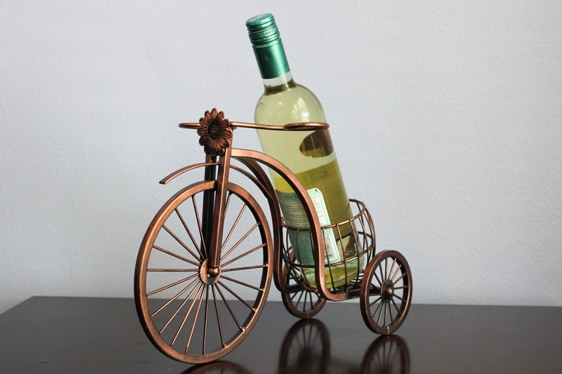 Bronze finish metal wine holder shaped like a bicycle, designed to display one wine bottle and two wine glasses in a charming and functional way, perfect for kitchen islands, dining rooms, wine stations, picnics, or outdoor entertaining, made from durable metal for long lasting use, serving as unique wine decor and a meaningful gift for weddings, anniversaries, housewarmings, holidays, and wine lovers who enjoy shared experiences