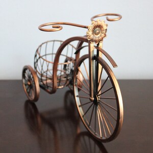 Metal wine bottle and glass holder crafted with a rich bronze finish and bicycle shaped design, holding one wine bottle and two glasses for easy serving, perfect for kitchen counters, dining spaces, wine displays, and outdoor picnics, built from durable metal for lasting quality, making it a standout wine decor piece and a thoughtful gift for couples, weddings, anniversaries, Valentine’s Day, holidays, and housewarming occasions