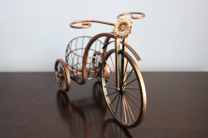 Metal wine bottle and glass holder crafted with a rich bronze finish and bicycle shaped design, holding one wine bottle and two glasses for easy serving, perfect for kitchen counters, dining spaces, wine displays, and outdoor picnics, built from durable metal for lasting quality, making it a standout wine decor piece and a thoughtful gift for couples, weddings, anniversaries, Valentine’s Day, holidays, and housewarming occasions