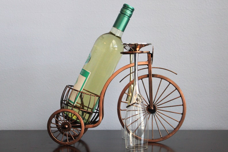 Unique metal wine and glass holder featuring a bronze finish and bicycle inspired design, created to hold one wine bottle and two glasses for easy sharing, ideal for kitchen counters, dining rooms, wine displays, and outdoor gatherings, crafted from sturdy metal for durability, and perfect as decorative wine holder decor, picnic wine display, or a thoughtful gift for weddings, anniversaries, holidays, and couples who appreciate functional yet creative home accents