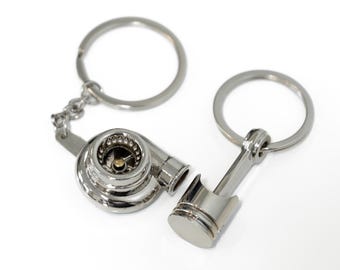 May include: A silver key chain with a turbocharger and a connecting rod charm. The turbocharger has a silver and gold finish and a detailed design. The connecting rod is a simple design with a silver finish.