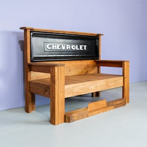 May include: Wooden bench with a black Chevrolet tailgate as a backrest. The bench is made of light brown wood and has a rectangular seat and armrests. The word "CHEVROLET" is visible on the tailgate.