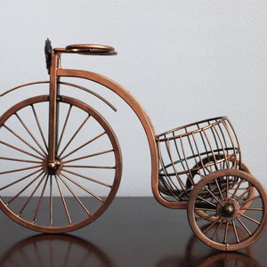 Bronze metal wine holder designed as a bicycle shaped display, holding one wine bottle and two wine glasses for shared moments, perfect for kitchen counters, dining areas, wine stations, or picnic setups, made from sturdy metal for durability, serving as unique wine decor and a conversation piece, and an excellent gift choice for weddings, anniversaries, holidays, Valentine’s Day, and housewarming gifts for wine lovers