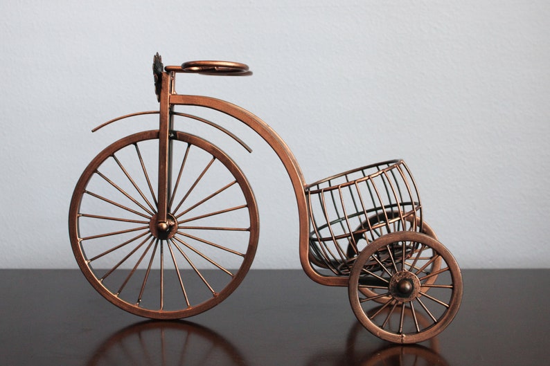 Bronze metal wine holder designed as a bicycle shaped display, holding one wine bottle and two wine glasses for shared moments, perfect for kitchen counters, dining areas, wine stations, or picnic setups, made from sturdy metal for durability, serving as unique wine decor and a conversation piece, and an excellent gift choice for weddings, anniversaries, holidays, Valentine’s Day, and housewarming gifts for wine lovers