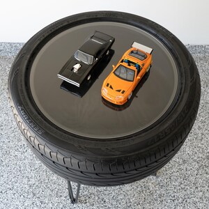 Bar-height tire table crafted from a real recycled tire, featuring a flush plexiglass top, solid wood base, and sturdy 24-inch metal legs, standing at 34 inches tall. This unique automotive table adds an industrial, modern touch to garages, man caves, bars, or home decor. Perfect as a high-top table, side table, or statement piece, it blends durability and style, making it a must-have for car lovers and those who appreciate repurposed furniture.