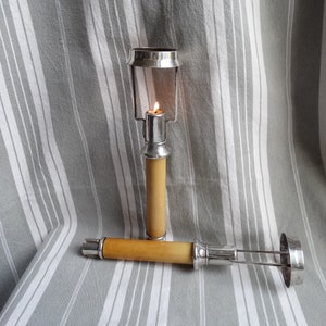 May include: Two silver candle holders with a wooden base. The candle holder on the left has a lit candle inside. The candle holder on the right is lying on its side.
