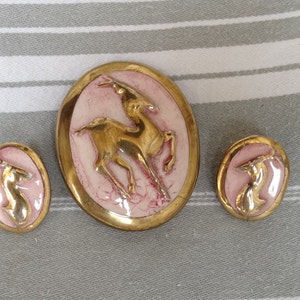 Peut inclure: Un ensemble de trois boutons en céramique dorés sur fond rose. Les boutons présentent un motif en relief d'un cerf stylisé en position de course.