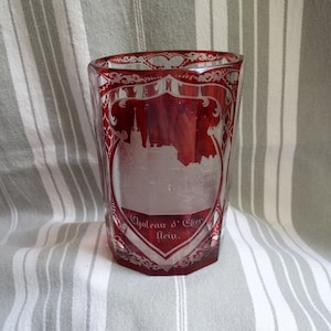 Op de afbeelding: Een rood glazen beker met een gegraveerd ontwerp van een kasteel en de tekst "Chateau d'Eber stein."