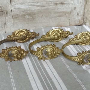 May include: Four ornate gold-toned metal curtain tiebacks with a decorative floral design.