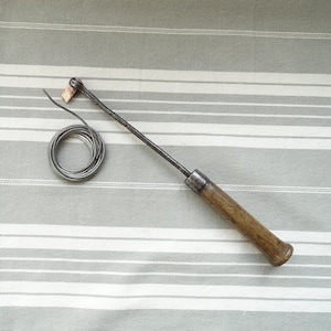 Puede incluir: Un soldador de metal con mango de madera y una bobina de alambre de soldadura sobre un fondo de tela a rayas.