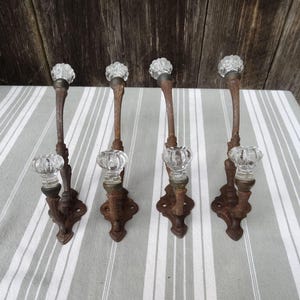 May include: Set of four antique rusty metal hooks with glass knobs. Each hook has a double hook design and a decorative base.