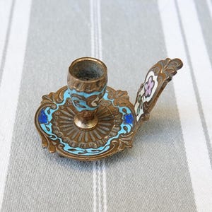 Peut inclure: Un petit chandelier en laiton orné avec un motif en émail bleu et blanc. Le chandelier a une poignée et une petite coupe pour tenir une bougie.