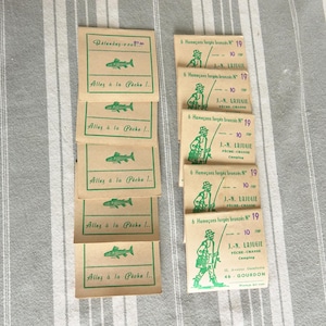 May include: A stack of small brown paper packets with green text and illustrations. The packets contain fishing hooks and have the text "Allez à la Pécha I.." and "J.-N. LAJUGIE PECHE-CHASSE Camping 21. Avenue Gambetta 46 GOURDON".