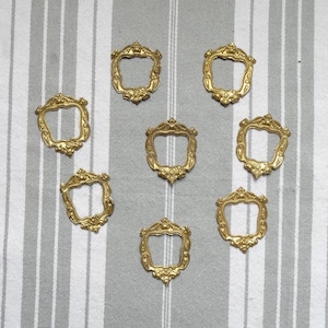 May include: Eight gold-toned metal decorative frames with ornate details. The frames are arranged in a circular pattern on a striped background.