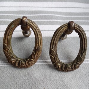 May include: Two antique brass oval cabinet pulls with a floral design. The pulls have a screw on the back for attaching to a cabinet door.