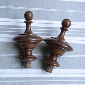 Può includere: Due tappi per bottiglie in legno tornito. I tappi sono di colore marrone scuro, con una parte superiore bulbosa e una base svasata. I tappi sono su uno sfondo a righe.