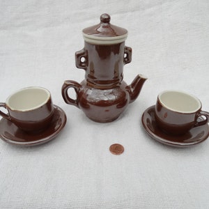 May include: A brown ceramic tea set with a teapot, two cups, and two saucers. The teapot has a lid and a handle on each side. The cups and saucers are plain.