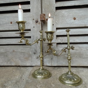 May include: A pair of antique brass candle holders with ornate details. Each holder features a single candle socket and a decorative base.
